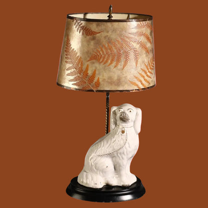 Decorative lamp with a ceramic dog base and leaf-patterned shade on a white background