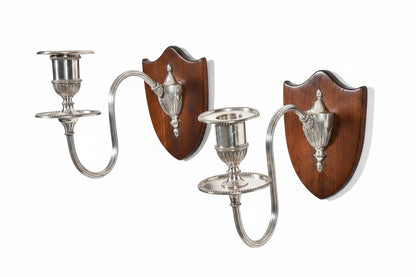 Two silver wall sconces with wooden backplates on a pegboard background