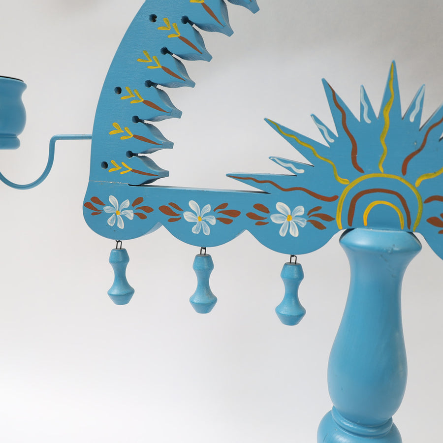 Close-up of blue Swedish painted wood candelabrum with floral and sun folk art details